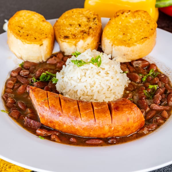 Cajun red beans and rice with sliced sausage and three pieces of garlic bread.