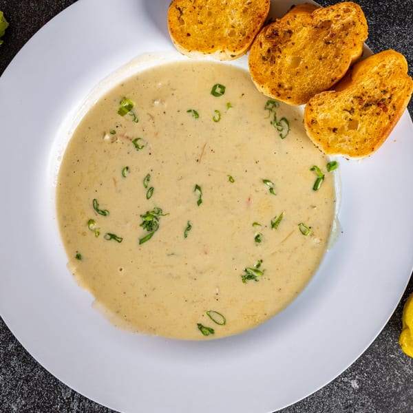Creamy Cajun soup with green onions and three slices of toasted garlic bread on a white plate.
