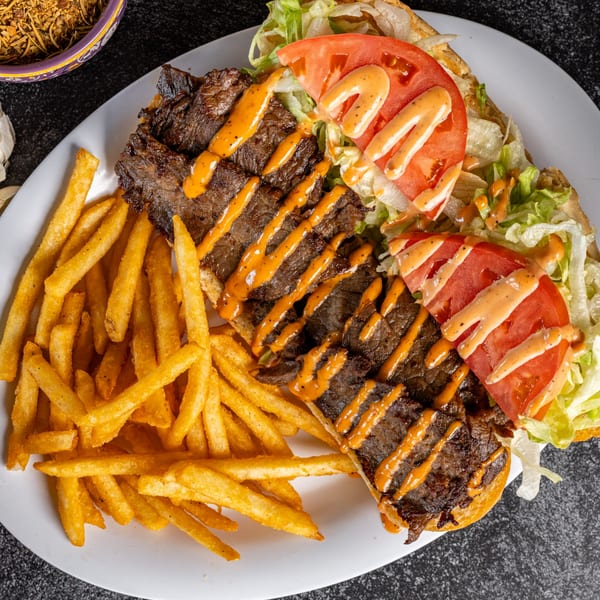 Cajun steak po'boy with lettuce, tomato, and sauce, served with a side of golden fries.