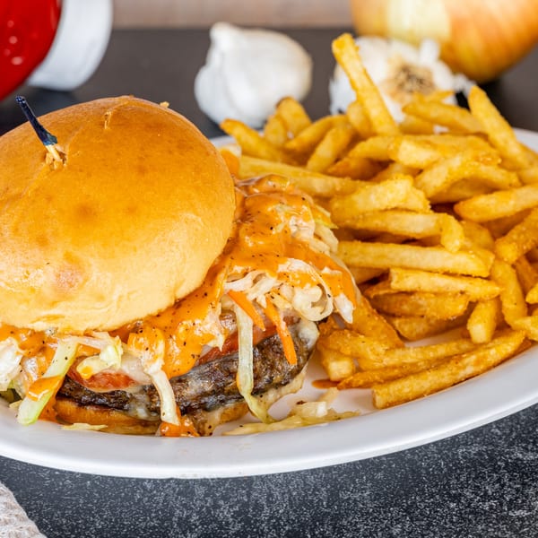 A Cajun burger with sauce and slaw, served with a side of golden french fries.