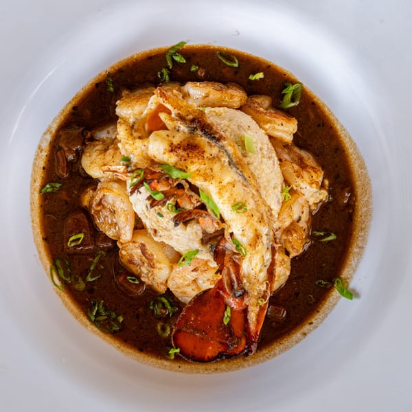 Cajun shrimp and grits with a lobster tail, dark gravy, and green onions in a white bowl.