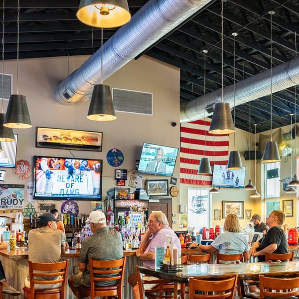 Patrons seated at the bar and tables inside Dat Cajun Place Cafe, watching sports on multiple TVs.