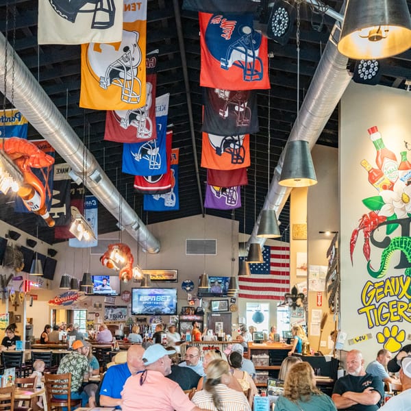 Dat Cajun Place Cafe interior with patrons, football flags, and Cajun-themed decor.
