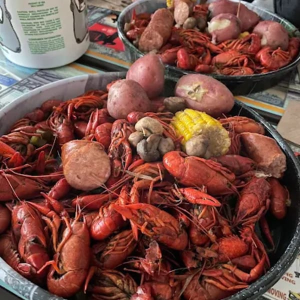 Two large bowls overflowing with boiled crawfish, potatoes, corn, mushrooms, and sausage.